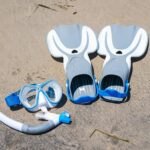 Close-up of snorkeling gear including fins and goggles on a sandy beach, ideal for summer activities.