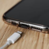 Modern cellphone in transparent cover with closeup of charging input and mobile phone white charger cable usb connector on wooden table